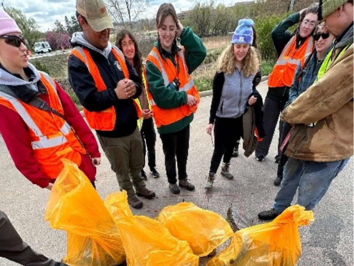 Students stand in a circle around several large yellow garbage bags.