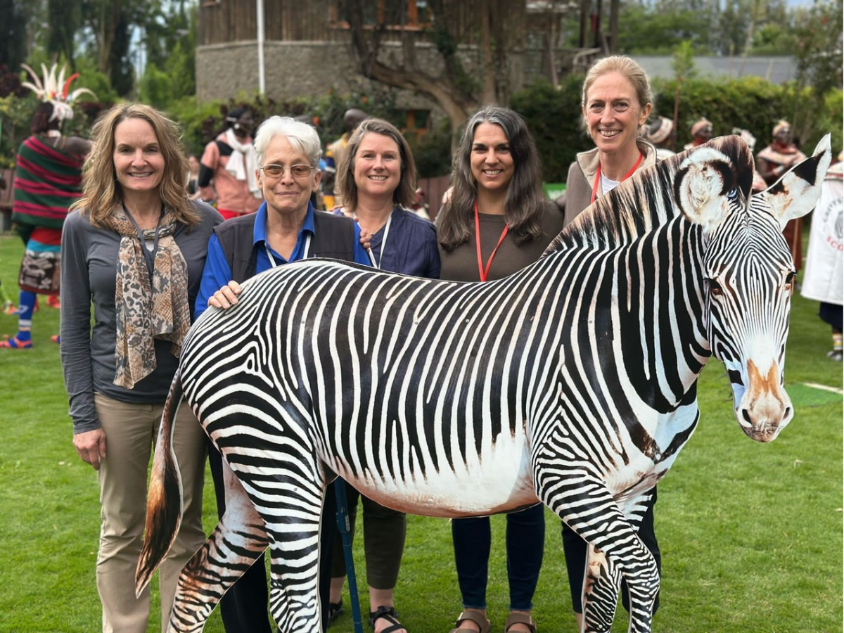 Five people stand behind a cut out of a zebra.