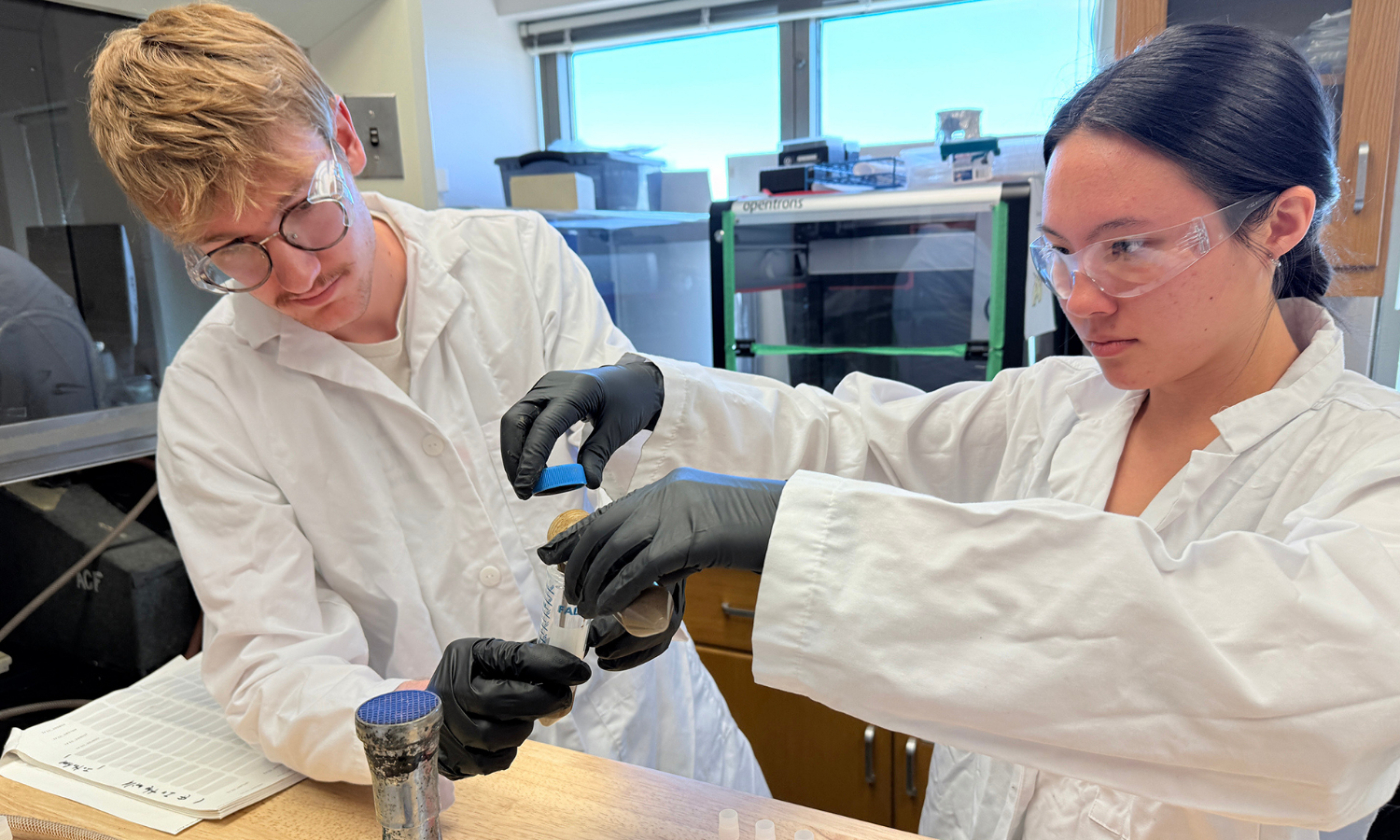 Two people in white lab coats test microbes in a laboratory. 