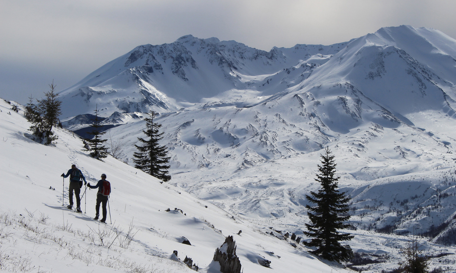 Two people snowshoe across a snowy mountain. 