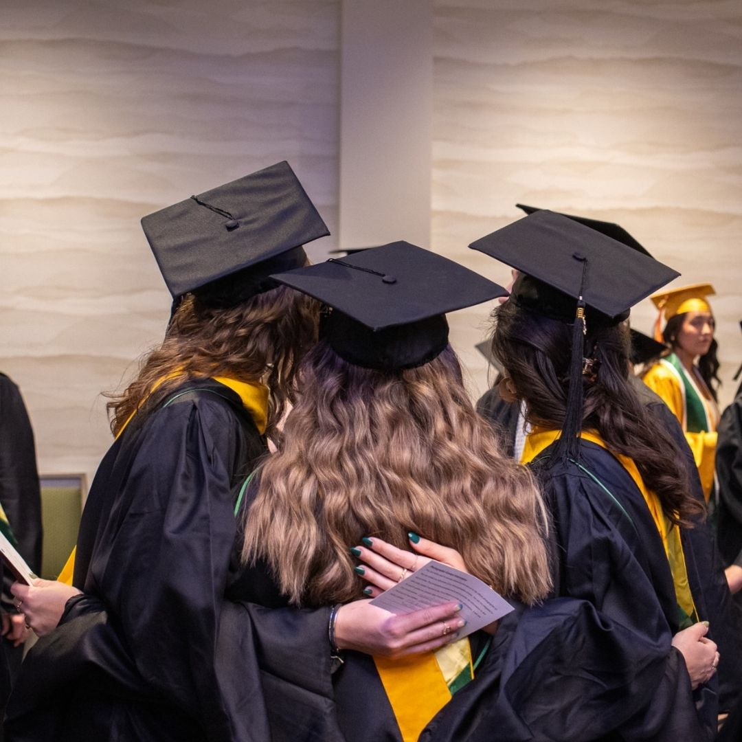 Three people hug in graduation regalia. 