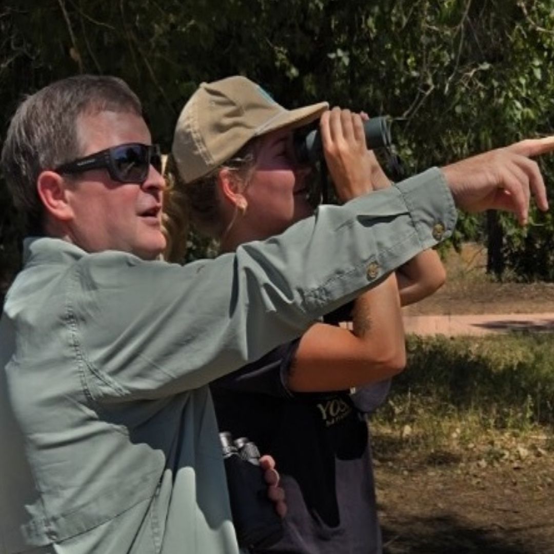 Paul Doherty points to something in the distance while a student looks through binoculars.