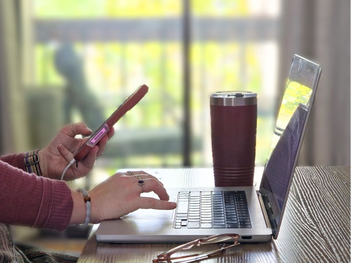 A person holds a phone while also typing on a computer. 