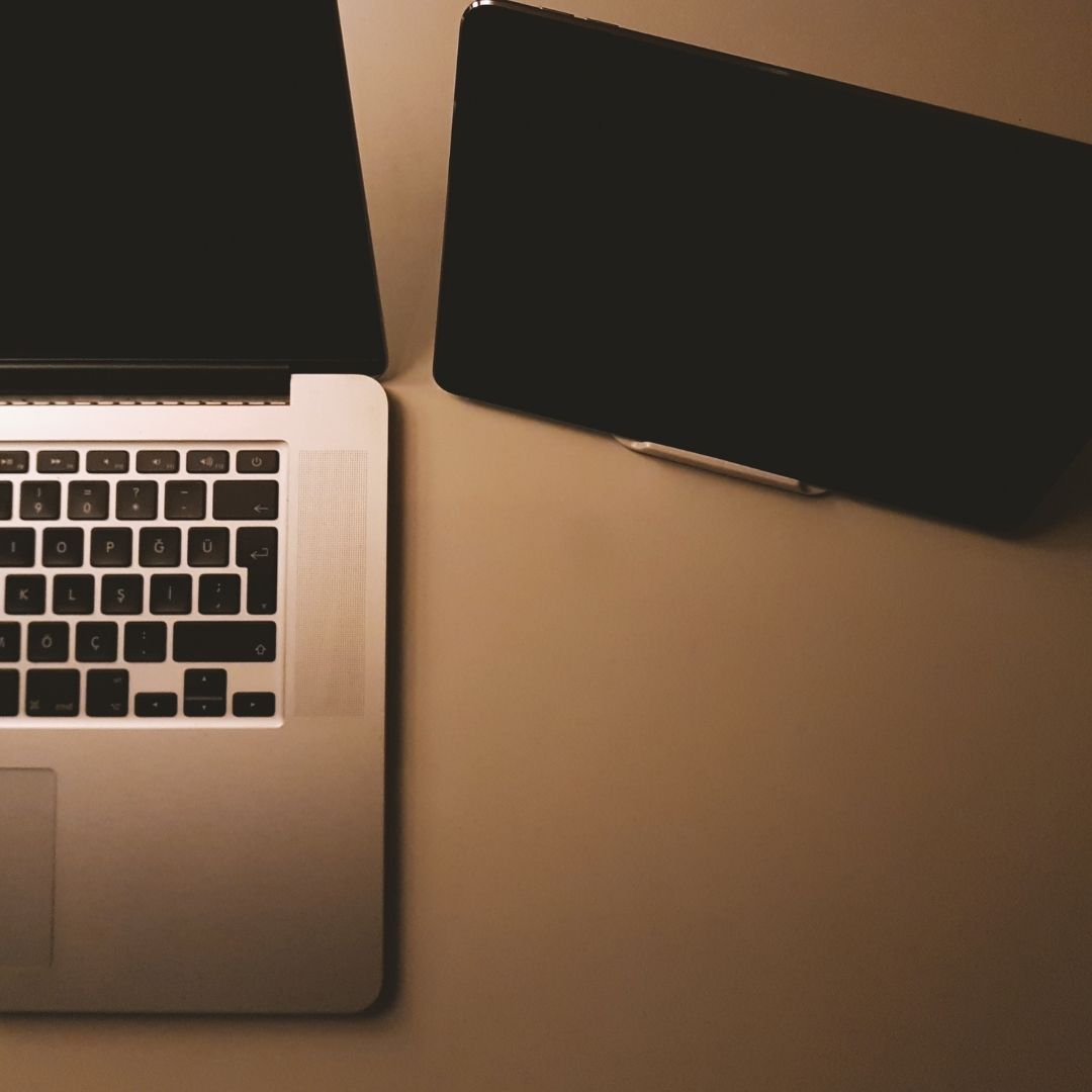 A laptop and a tablet sit next to each other on a table. 