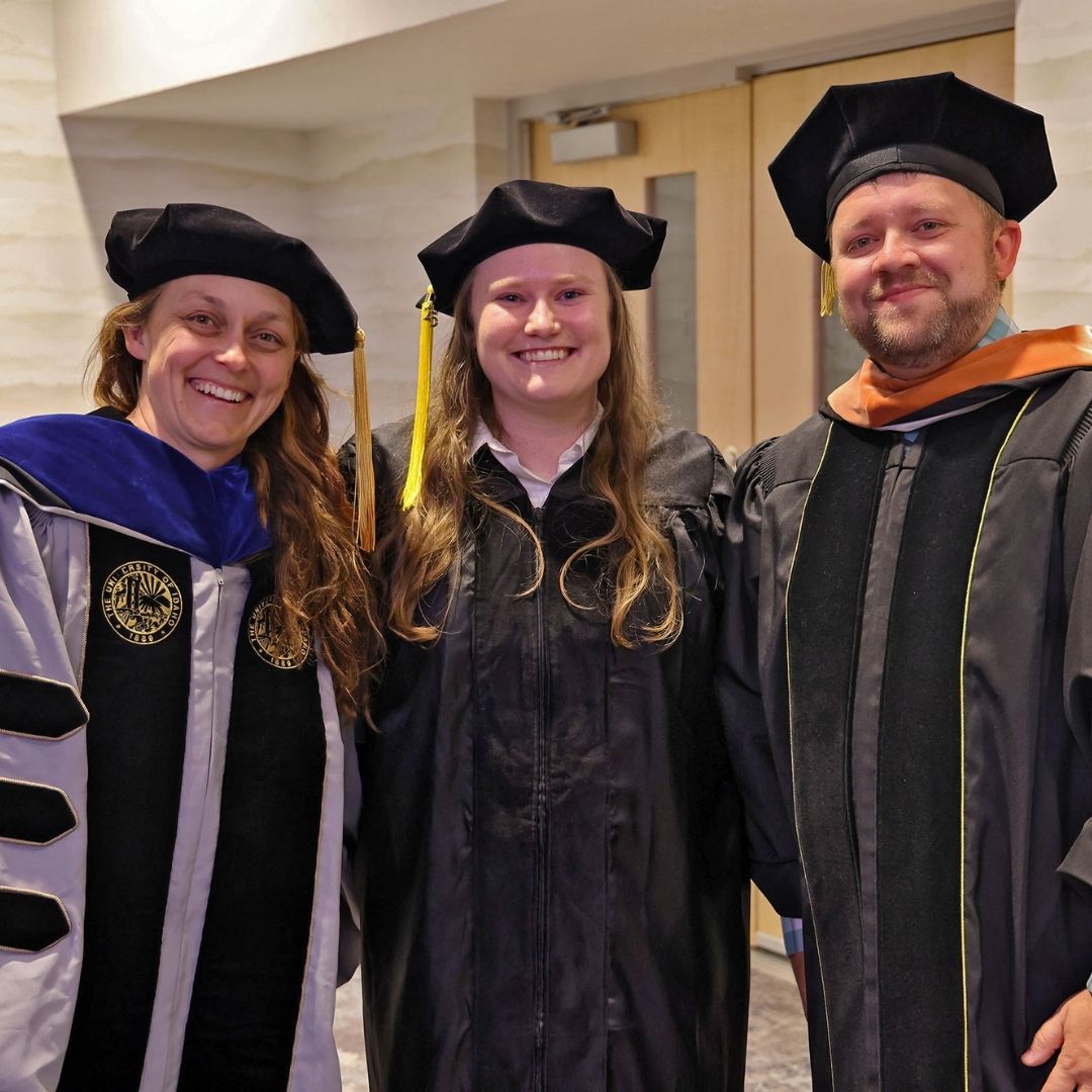Three people pose for a picture dressed in graduation regalia