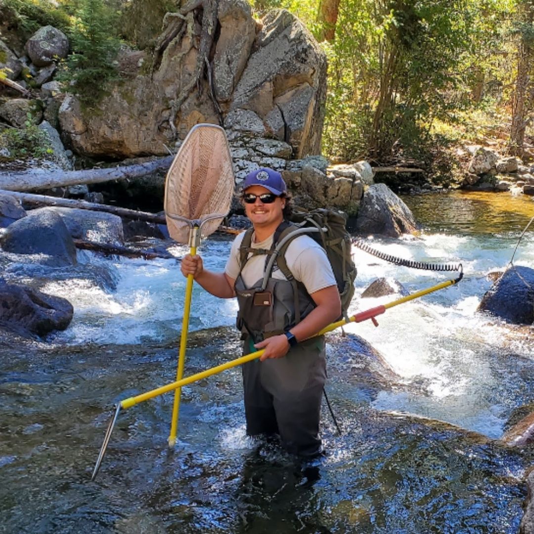 Kade Jackson holds a fishing net and a pole while standing in a river. 
