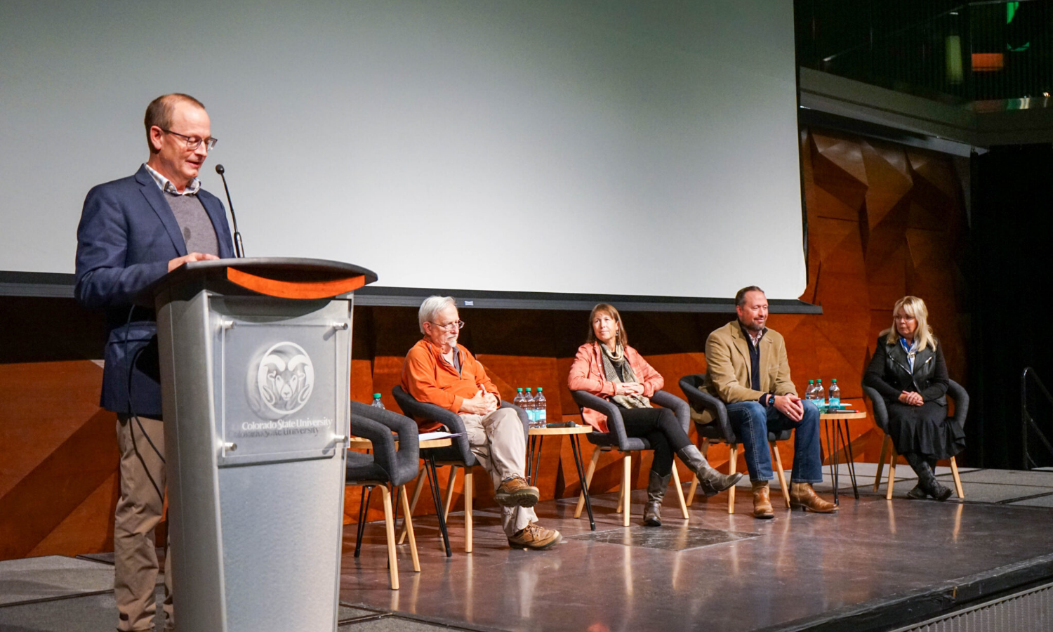 Person giving a speech at a podium with panelists in the background