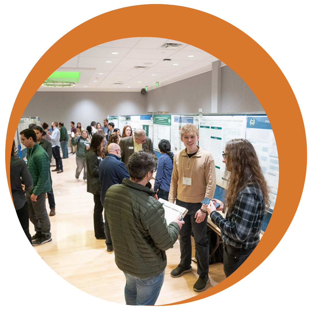 photo of graduate students standing in front of poster boards and presenting their work