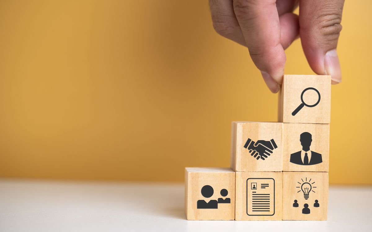 a person's hand building with wooden blocks that have human resources icons