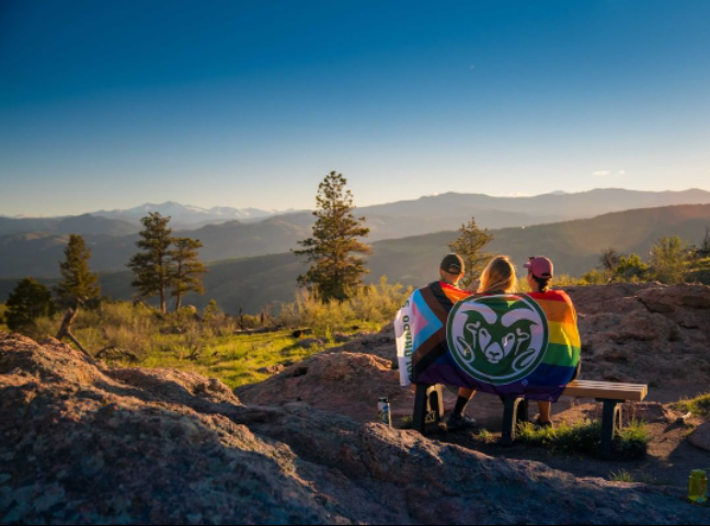 Three students in the mountains with CSU rainbow flag wrapped around them