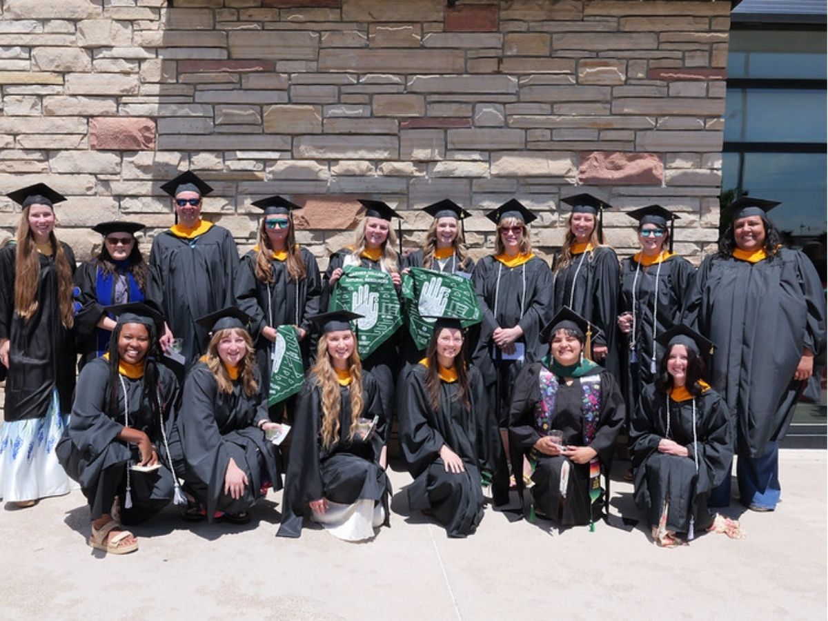 A group of graduates pose for a picture in front of a stone wall. 