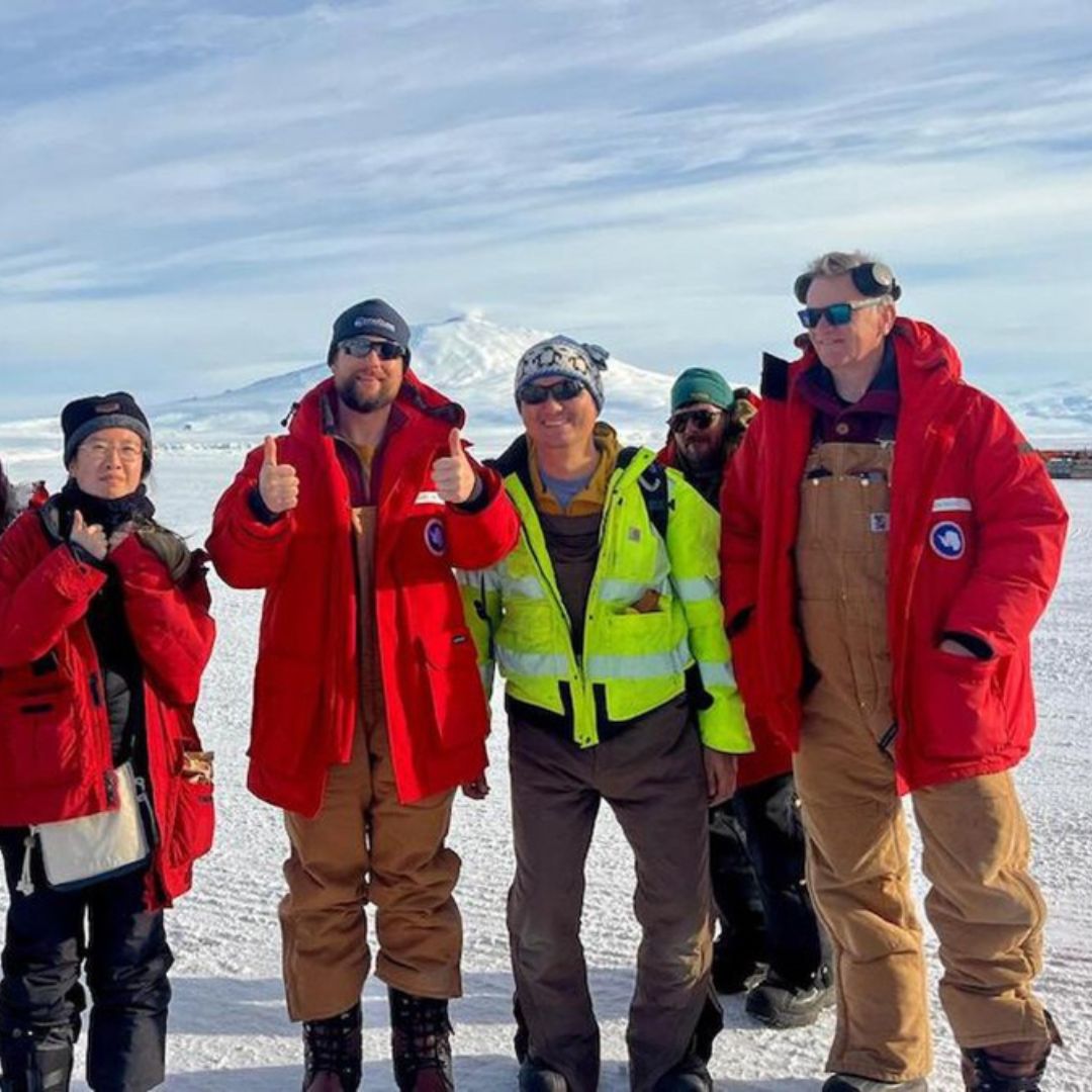 A group of people pose for a picture at the South Pole. 