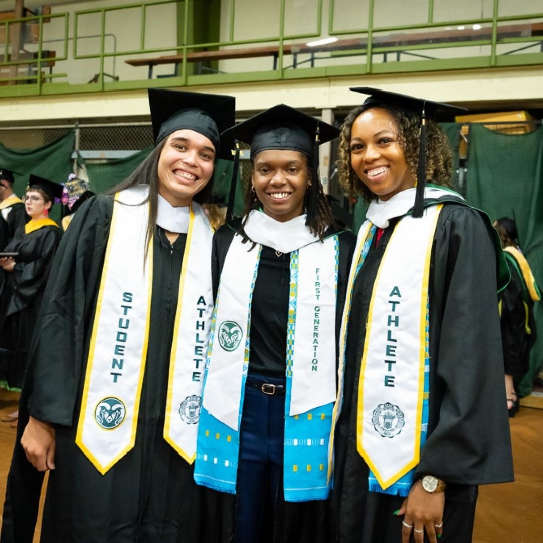 Three people hug in graduation regalia. 