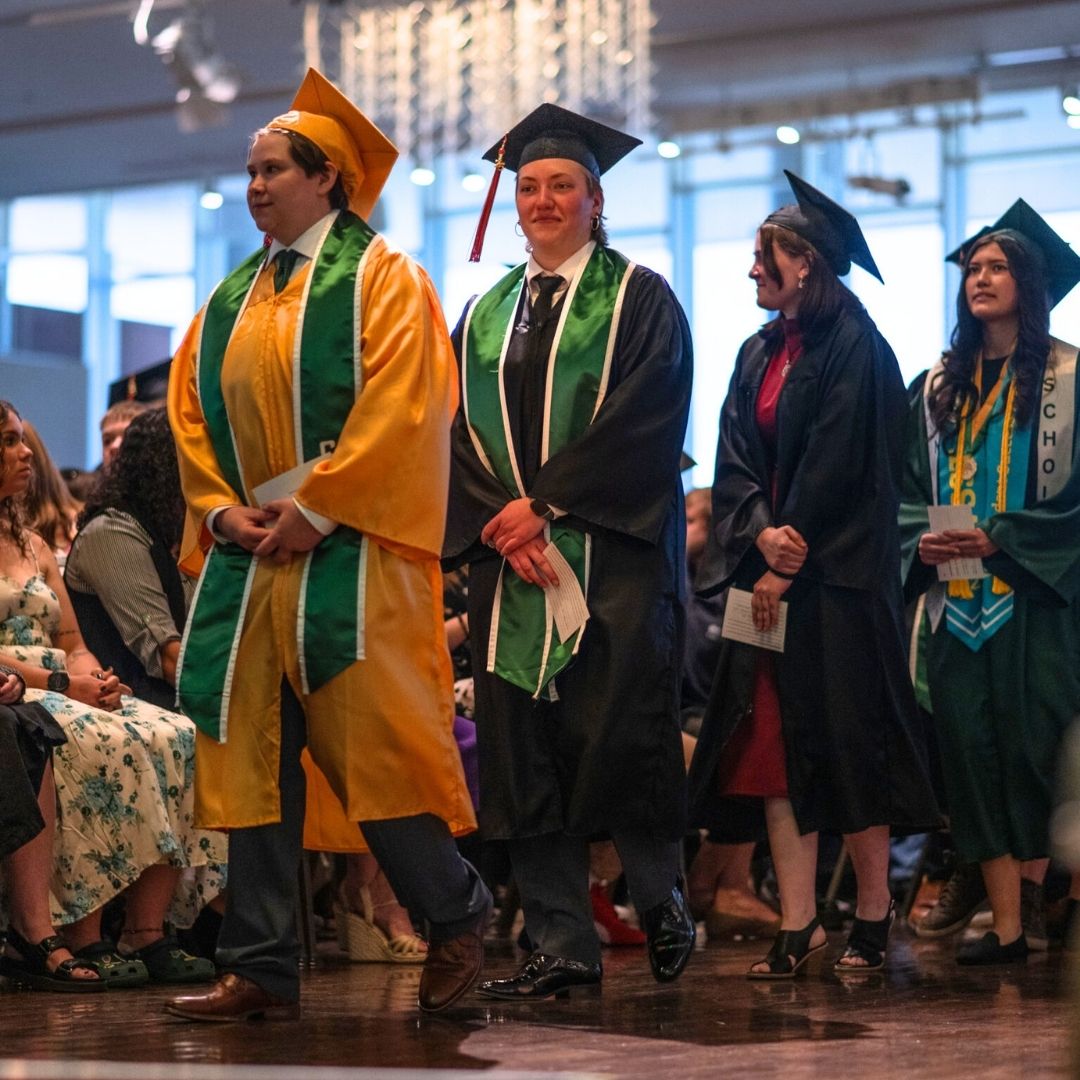 Students in commencement regalia walk in line.