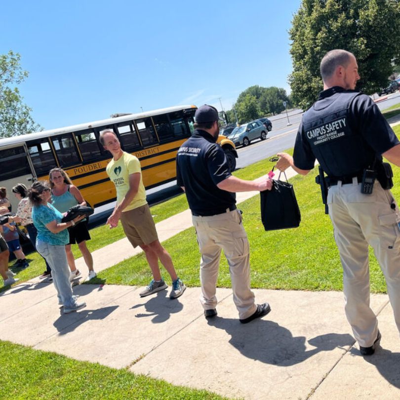 People stand in a line passing along backpacks to load onto a yellow school bus. 