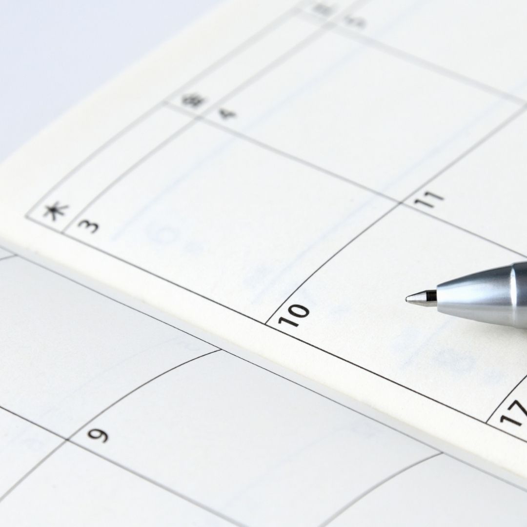 A pen sits on top of an open calendar. 