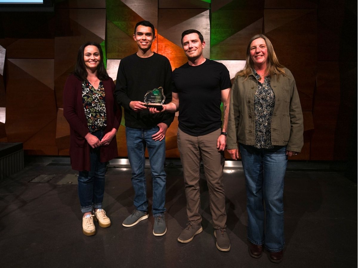 Four people pose for a photo, one of them holding an award