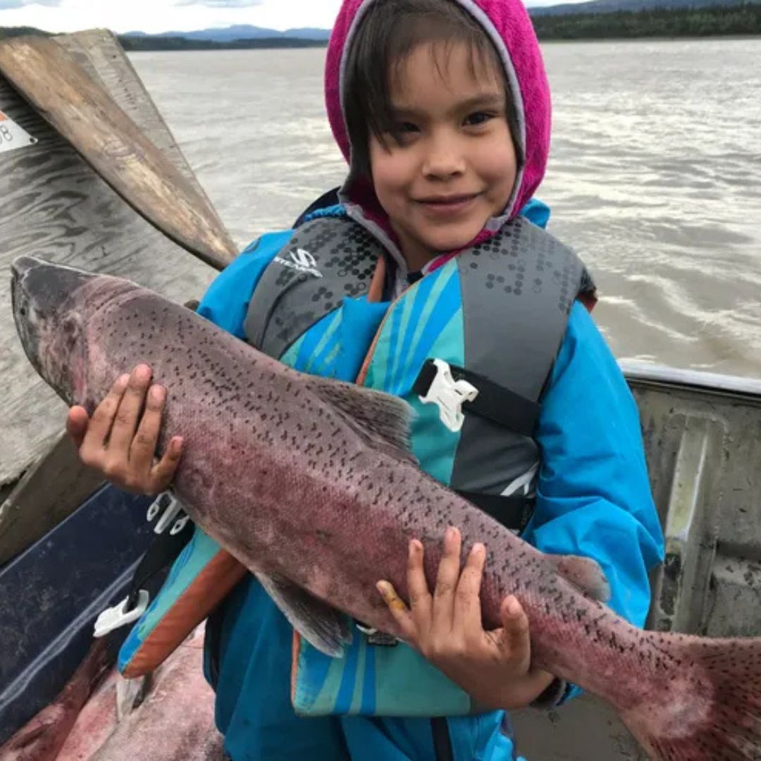 A child holds a large salmon on a boat.
