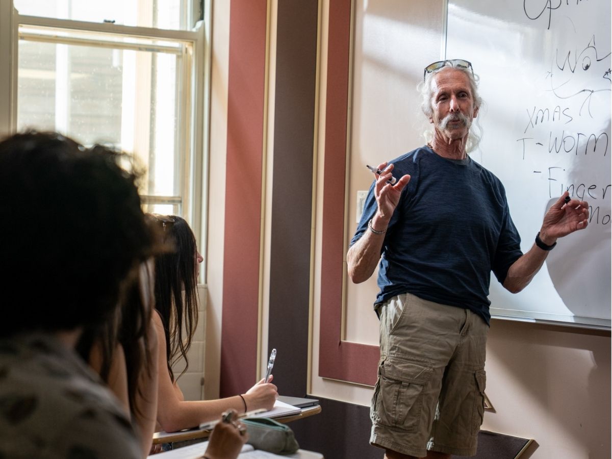 A professor stands at a white board teaching a class. 