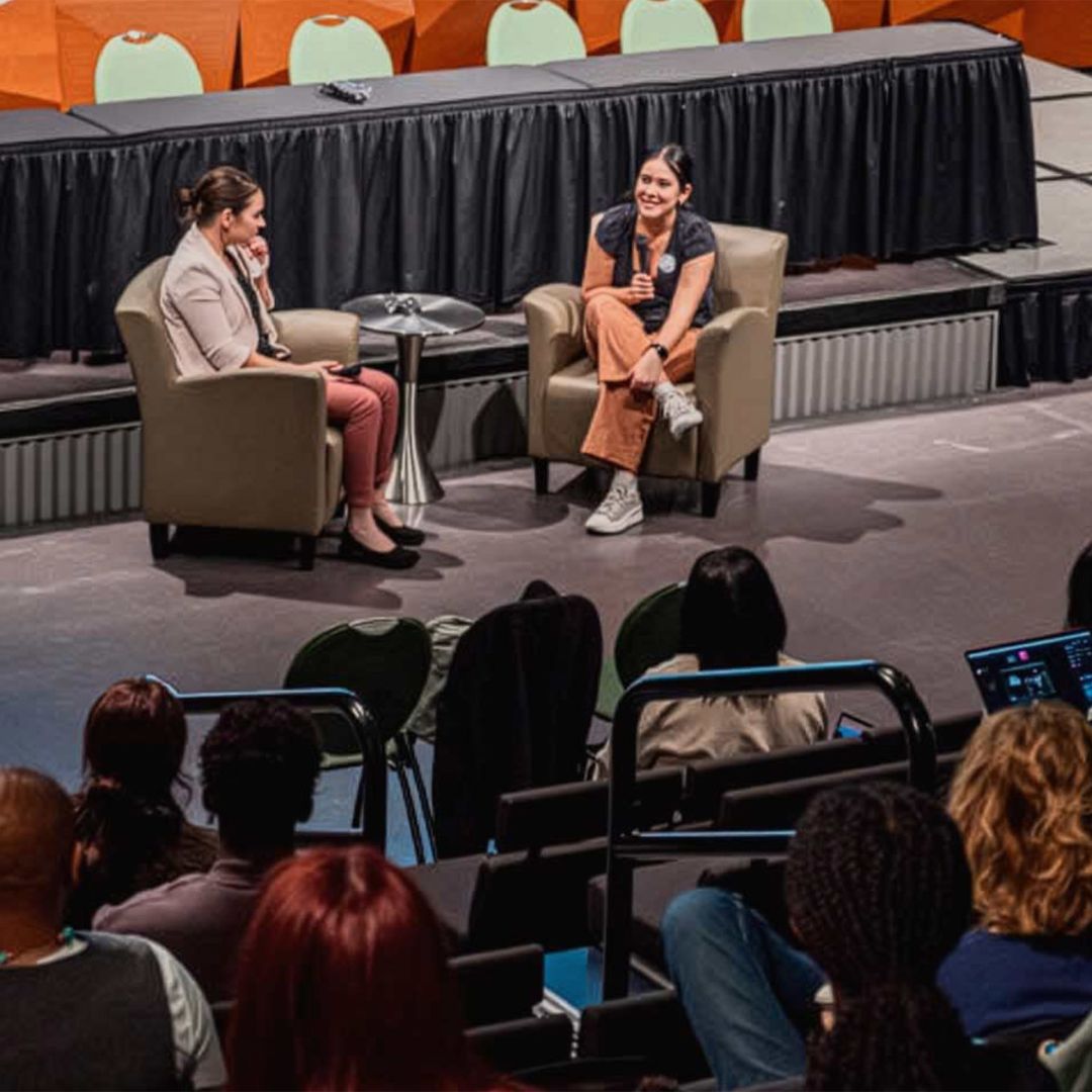 Two people sit on stage talking.
