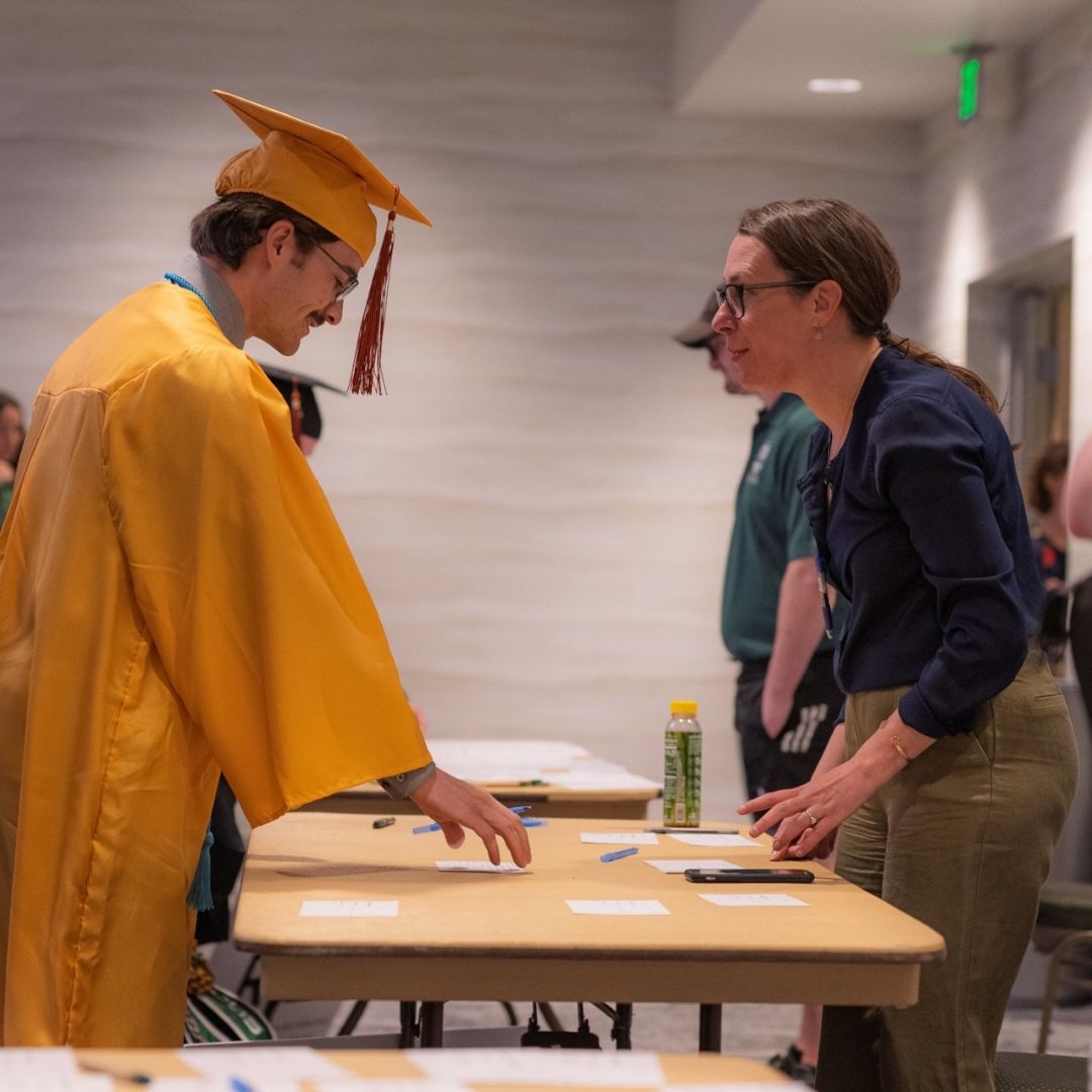 A person helps a graduate with their name card. 