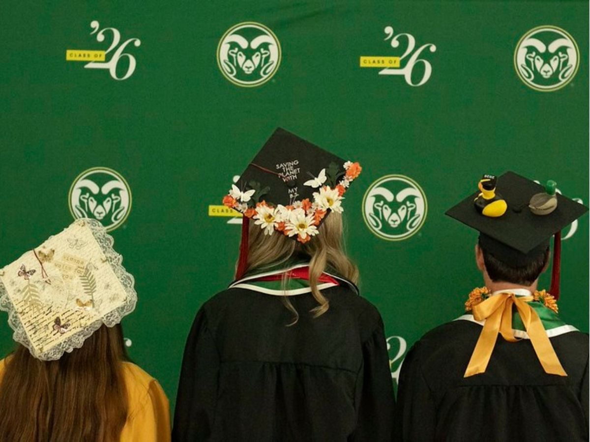 Three graduates face a green wall showing off their mortarboards. 