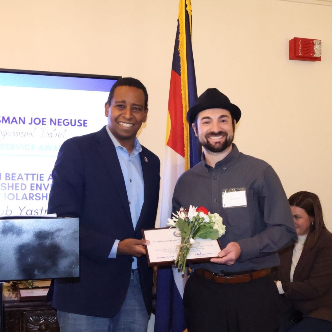 Photo of Jacob Yastrow holding an awards with Representative Joe Neguse