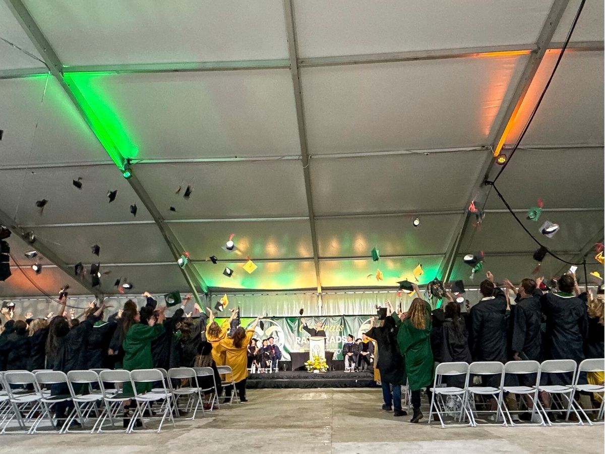 A large group of graduates throw their mortarboards in the air. 