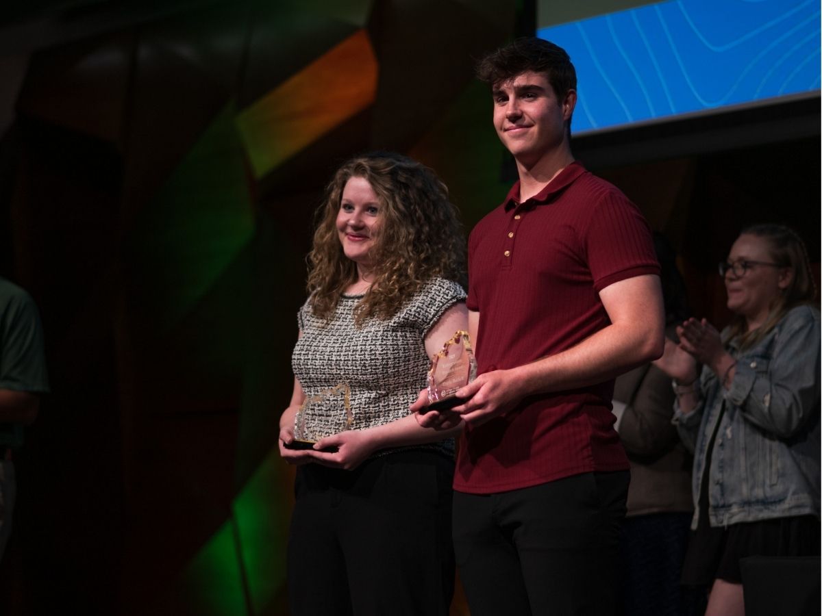 Two students stand on stage accepting awards. 