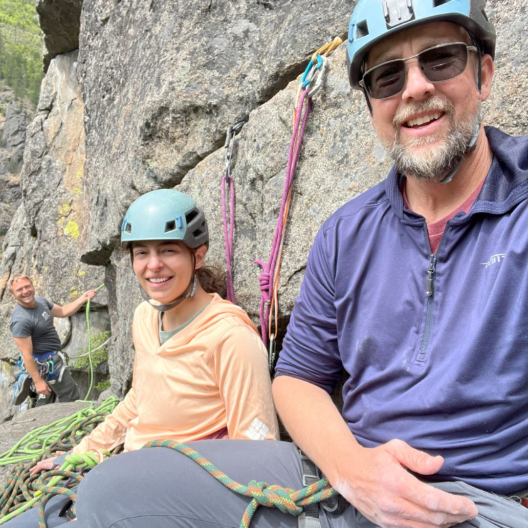 Three people pose for a picture while rock climbing. 