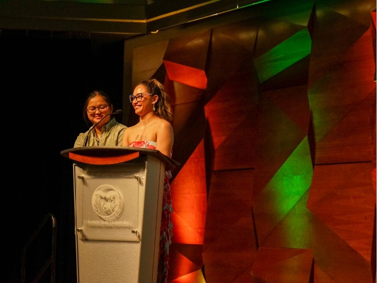 Two students stand at a podium speaking to the audience 
