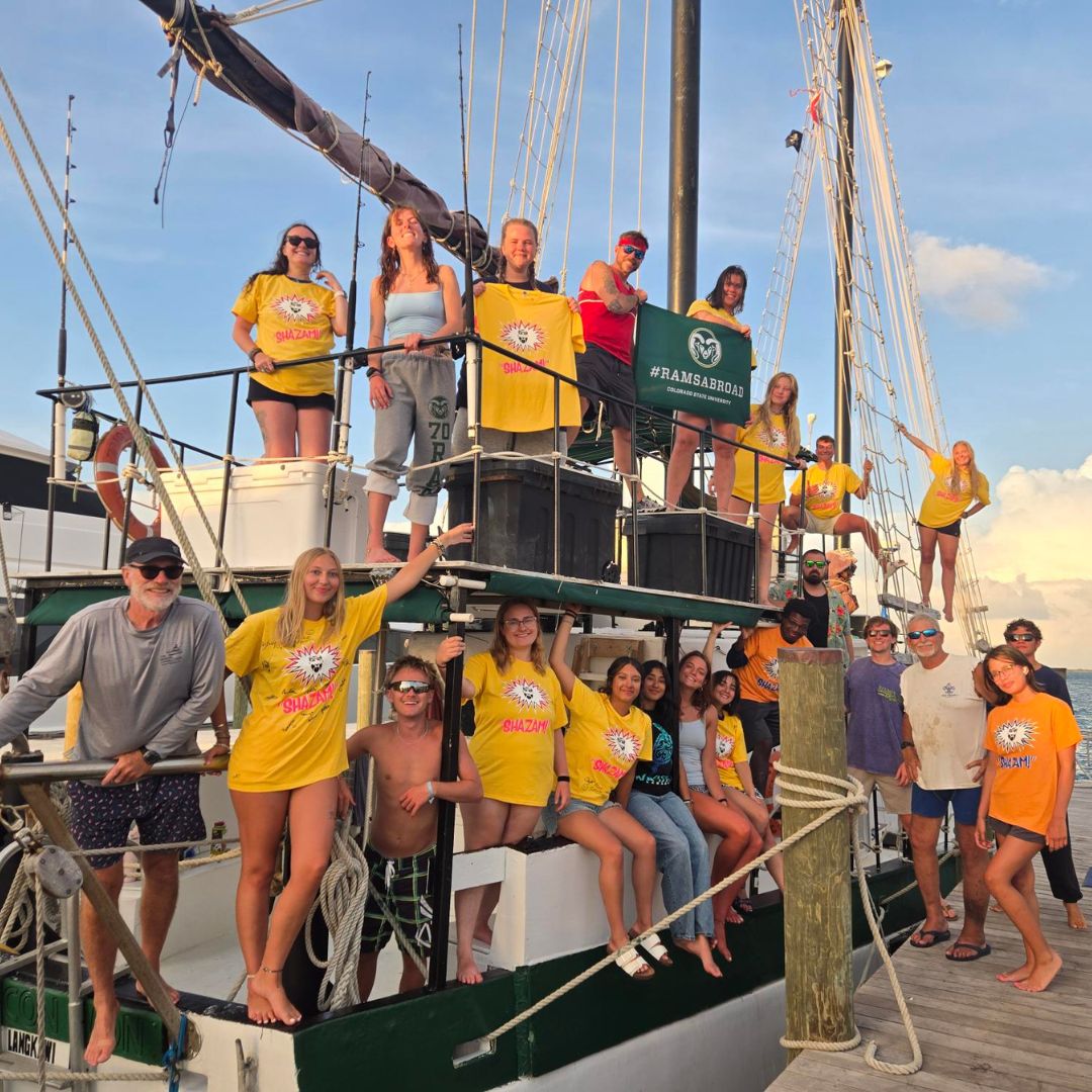 A group of students stand on a docked boat. 