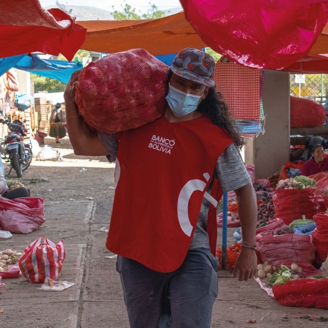 Dario carries a heavy bag over his shoulder while wearing a mask.