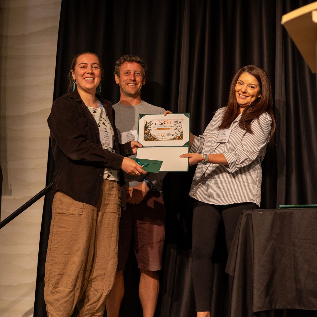 Three people stand on a stage holding an award.