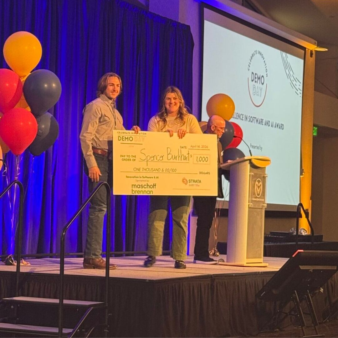 Two people stand on a stage holding a giant check for $1,000.O