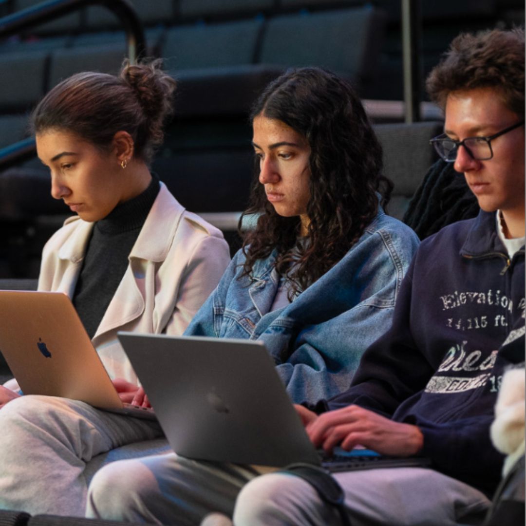 Three people sit in a row looking at their laptops. 