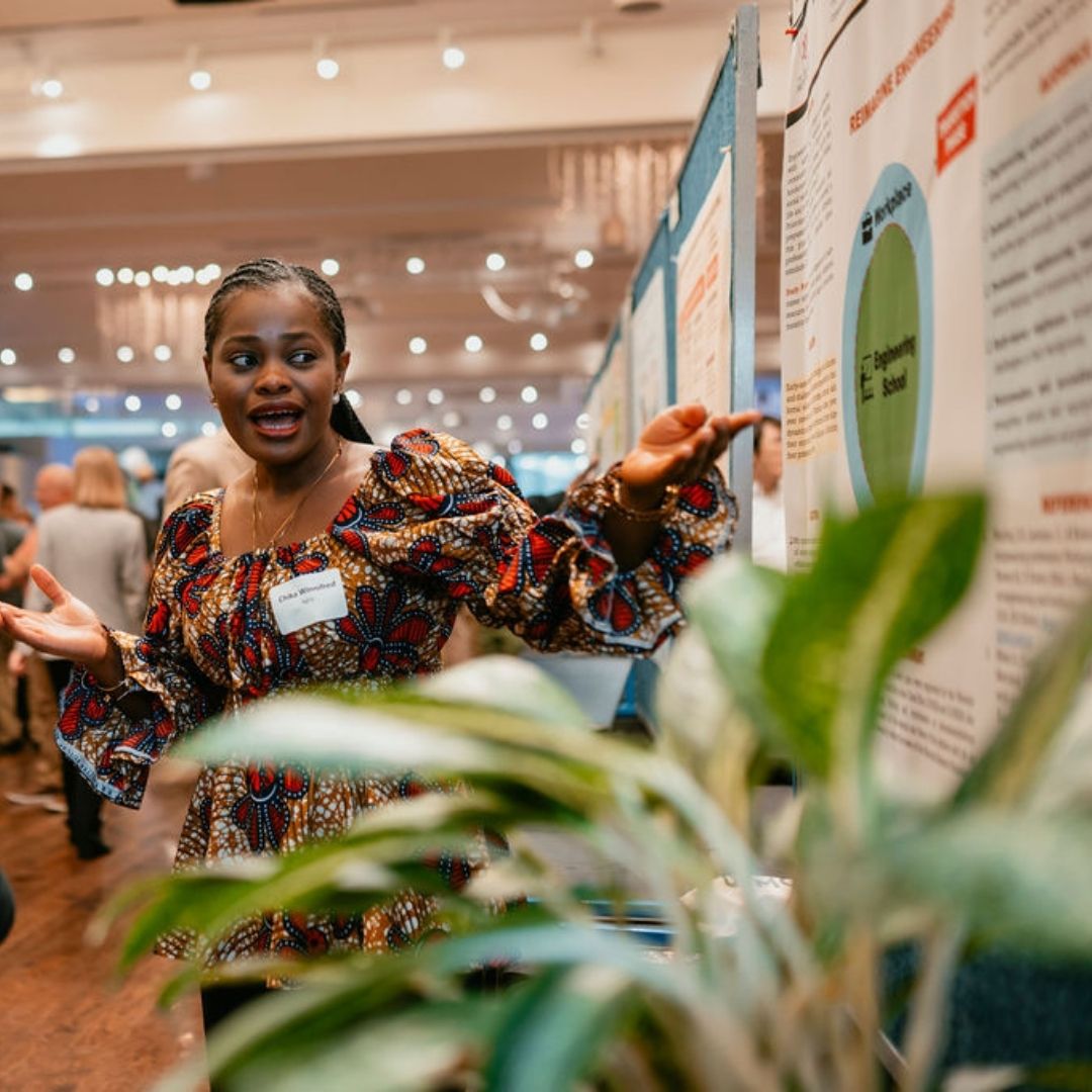 A student stands in front of their poster at the Grad Student Showcase